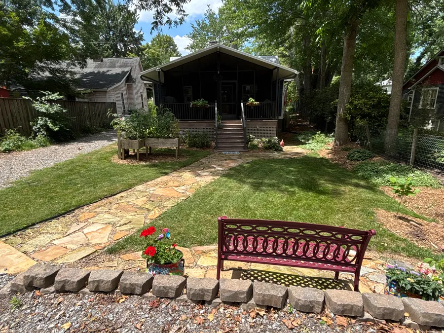 Residential front yard with a stone walkway, bench, lawn, porch, and edged planting beds.